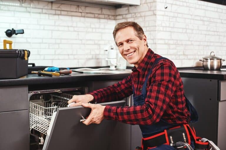call professional male technician sitting near dishwasher smiling