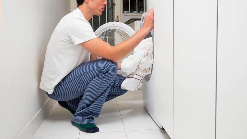 close up man putting clothes washing machine