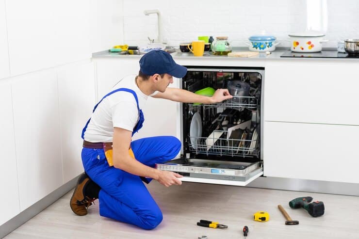 happy master male technician sitting near dishwasher with screwdriver kitchen with instruments smiling